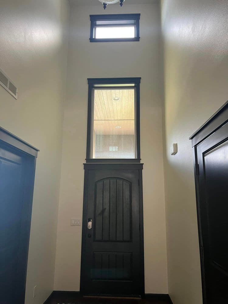 Modern entryway with tall ceilings, large window, and dark wooden door. Bright and spacious design.