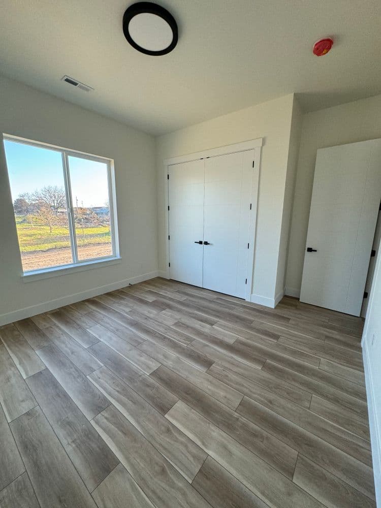 Bright, empty room with large windows, modern wood flooring, and closet doors.