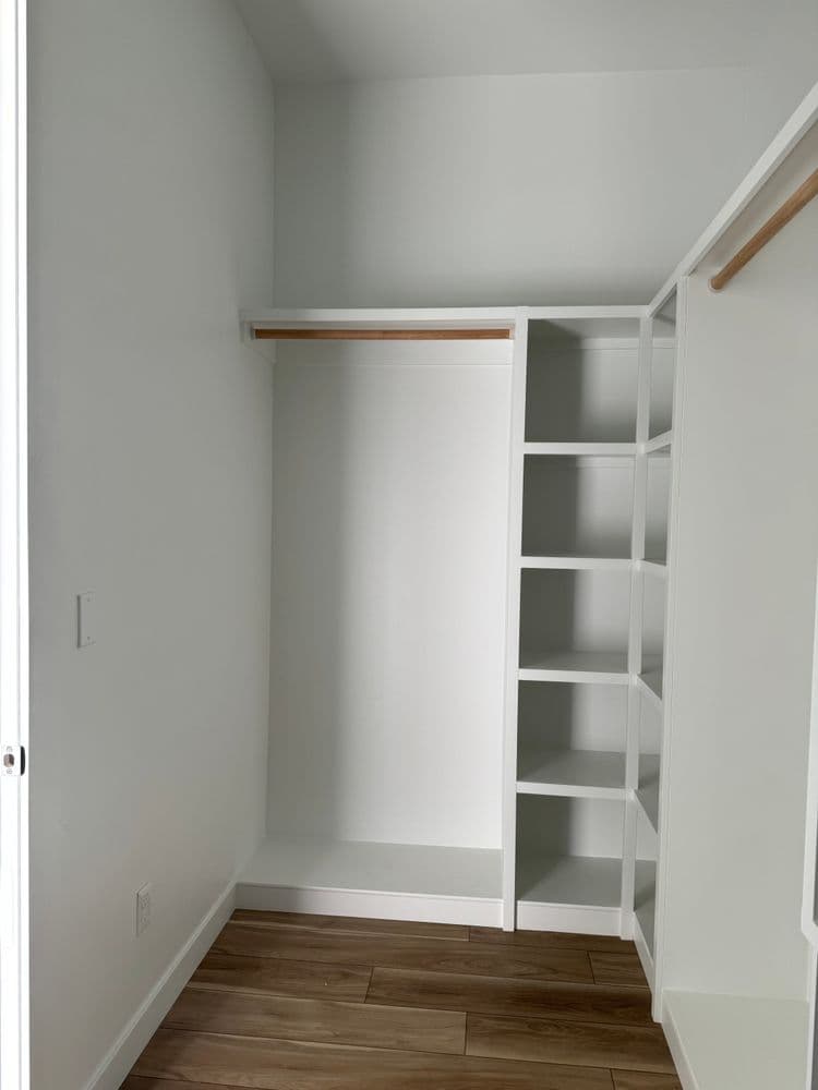 Empty modern closet with built-in shelves and hanging rod on light wall background.