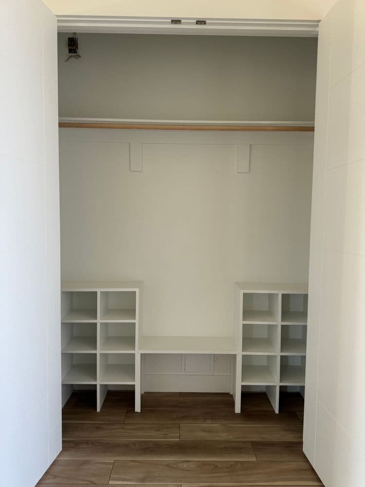 Empty closet with white shelving units and wooden floor, showcasing organized storage space.