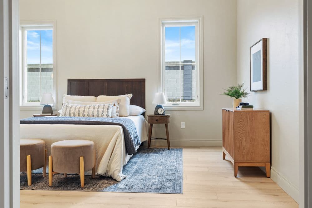 Modern bedroom with a queen bed, wooden furniture, and natural light from windows.