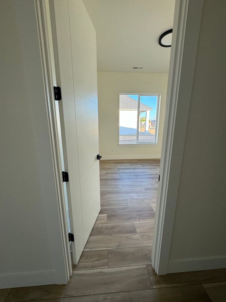 Interior view of a doorway leading to a bright, modern room with large windows and hardwood floors.