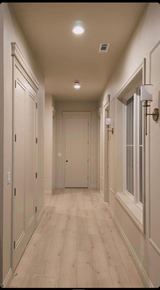 Modern interior hallway with light wood flooring, sconces, and white paneling.