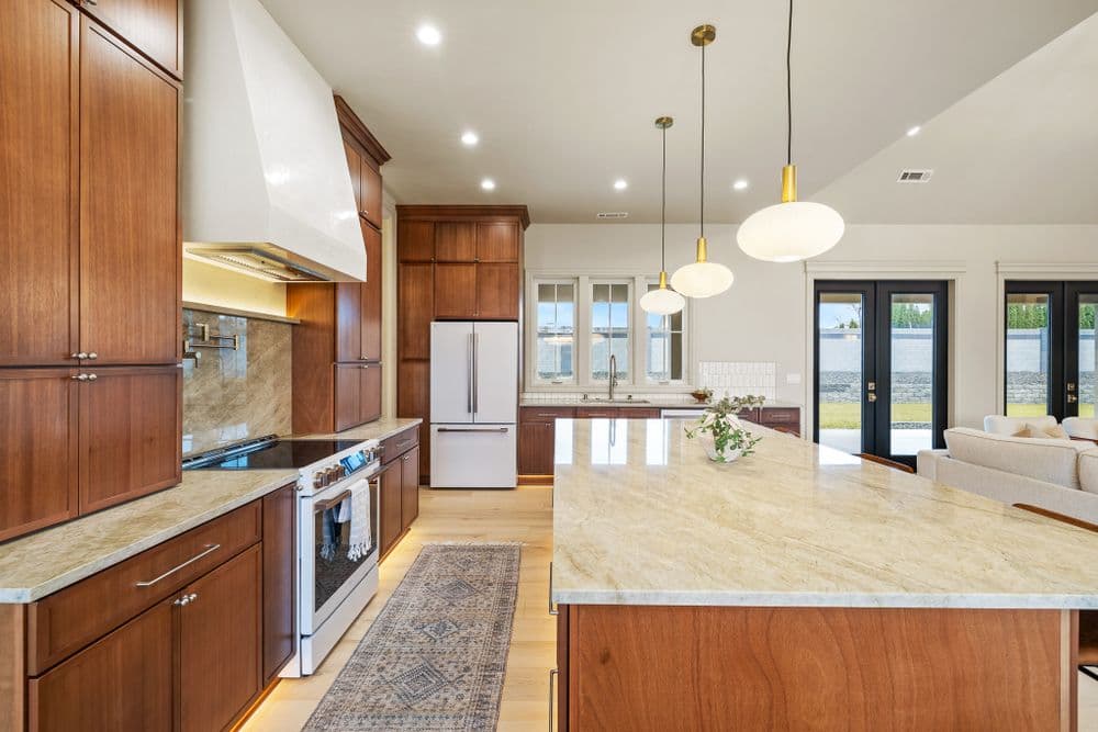 Modern kitchen with wooden cabinetry, marble countertops, and large windows showcasing a scenic view.