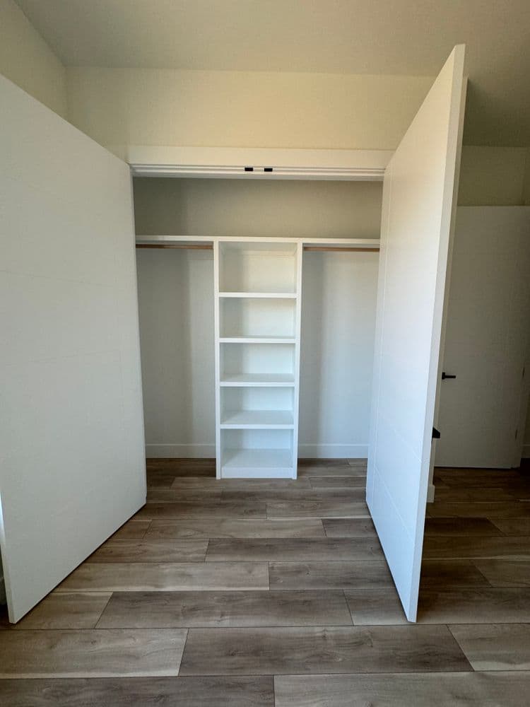 Modern open closet with white shelves and wooden flooring, showcasing organized storage space.