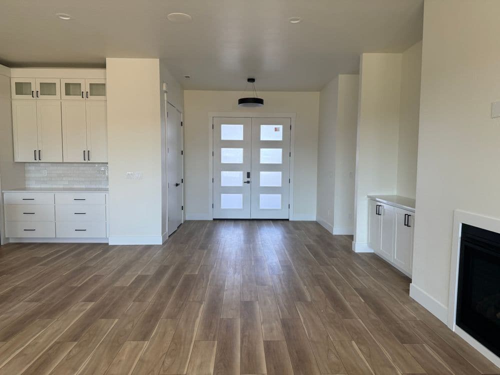 Modern living room with hardwood floors, white cabinets, and large front door.
