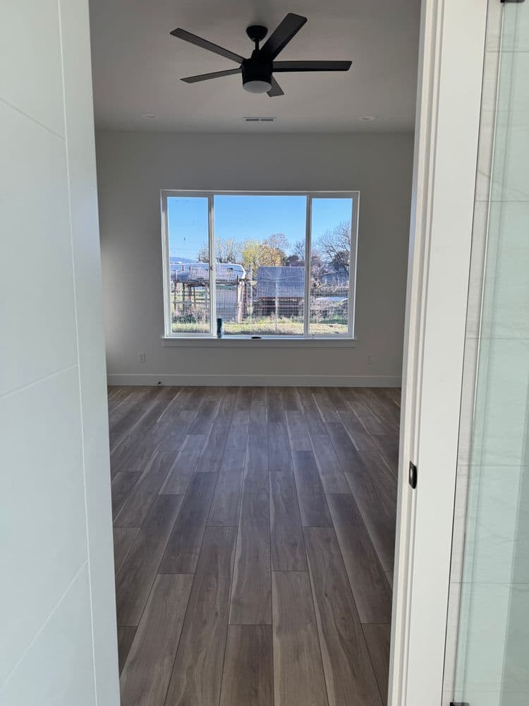 Spacious interior view of a room with wood floors and large windows overlooking a garden.