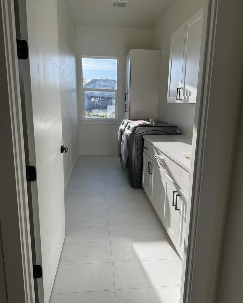 Bright laundry room featuring modern appliances, white cabinetry, and natural light from window.