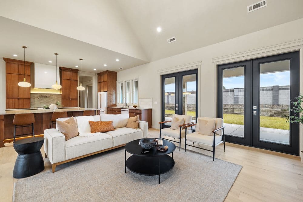 Modern living room with stylish furniture, large windows, and open kitchen layout.