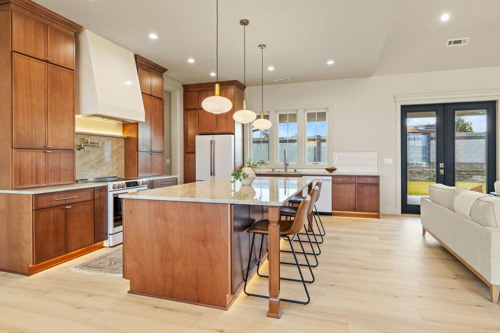 Modern kitchen with wooden cabinets, granite island, and sleek bar stools, featuring natural light.