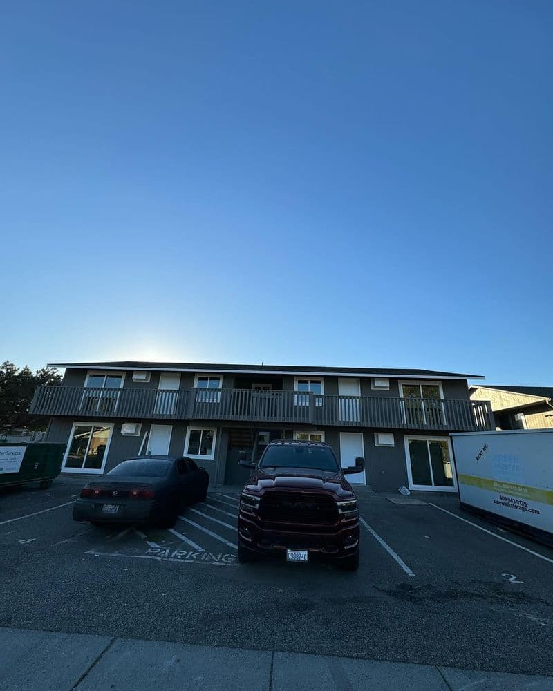 Two parked vehicles in front of a two-story apartment building under a clear blue sky.