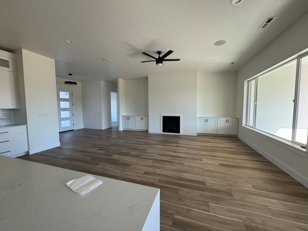 Spacious modern living room with fireplace, ceiling fan, and large windows.