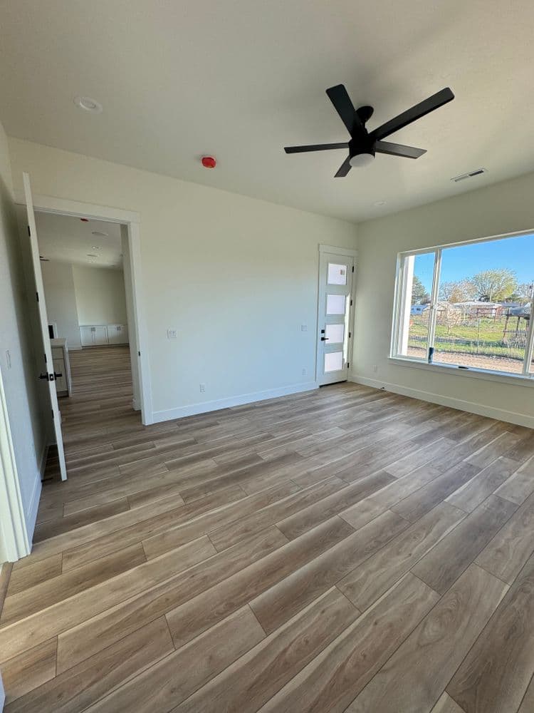 Bright, modern room with large windows, wood-style flooring, and ceiling fan.