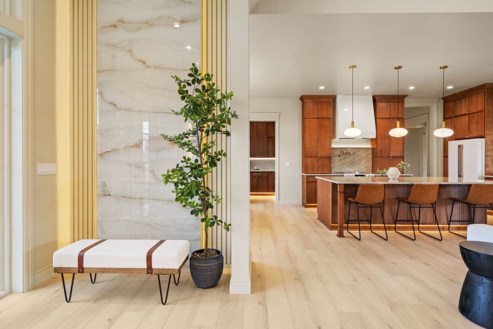 Modern interior with a stylish bench, greenery, and a spacious kitchen with wooden cabinetry.