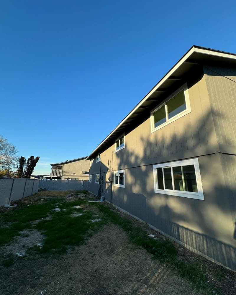 Side view of a modern gray house with windows and a clear blue sky in the background.