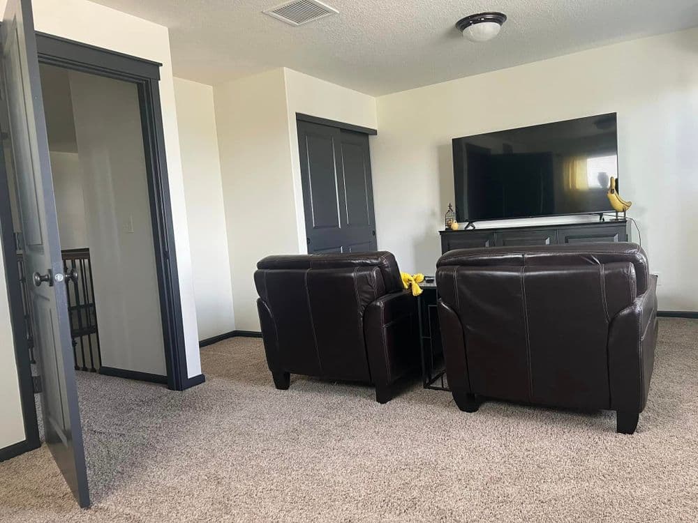 Cozy living room featuring two brown leather chairs and a large TV on a modern stand.