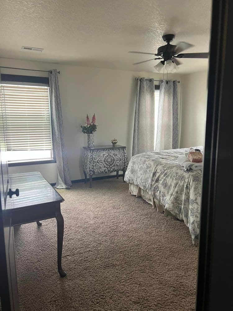 Cozy bedroom with floral bedding, a decorative table, and natural light from windows.