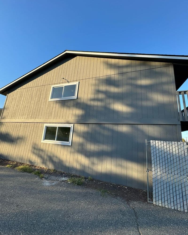 Two-story gray house exterior with windows, located on a clear blue sky day.