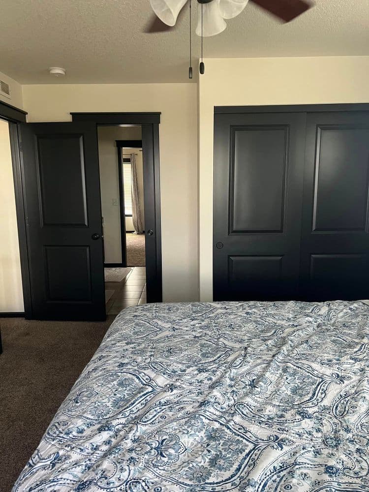Bedroom with a patterned blue bedspread and dark double doors leading to another room.