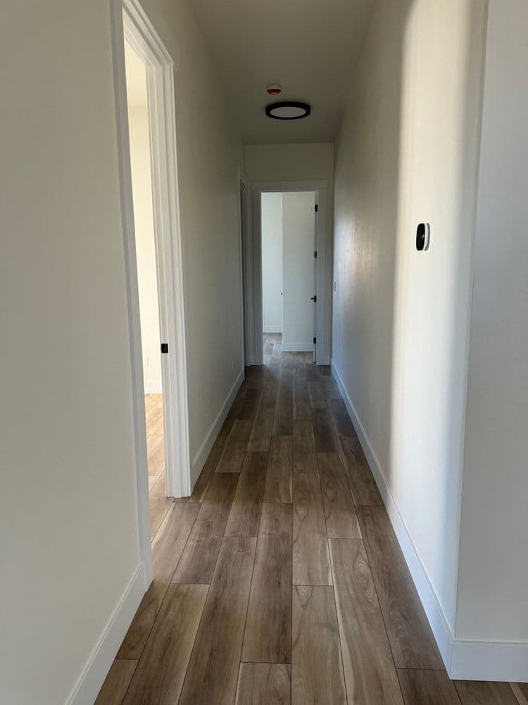 Modern hallway with wooden flooring, white walls, and doorways leading to rooms.