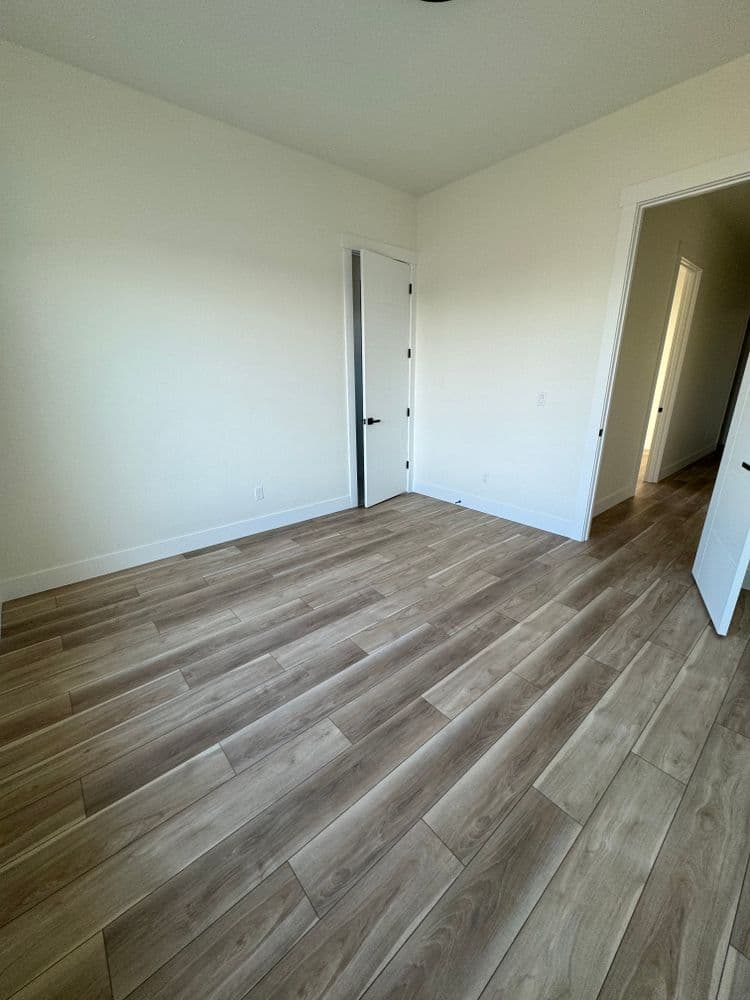 Empty room with light-colored walls and wooden flooring, featuring a closed door and natural light.
